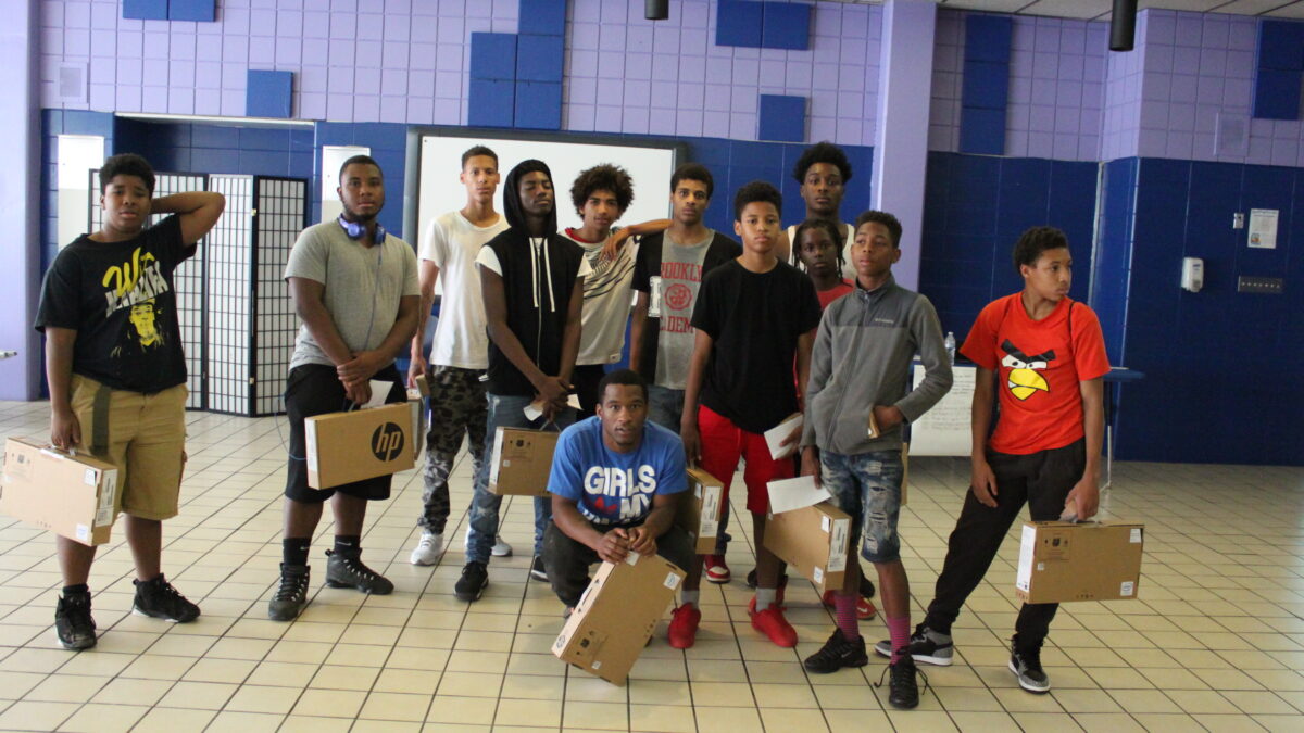 Twelve teens holding laptop computers still in cardboard boxes