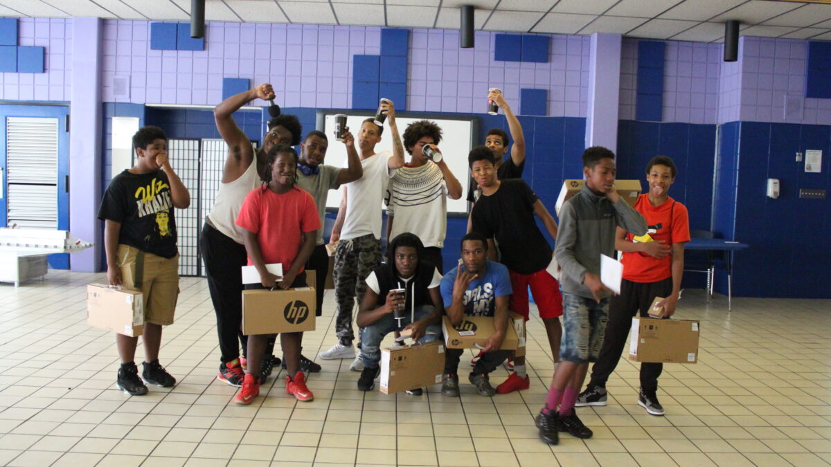 Twelve teens holding laptop computers still in cardboard boxes