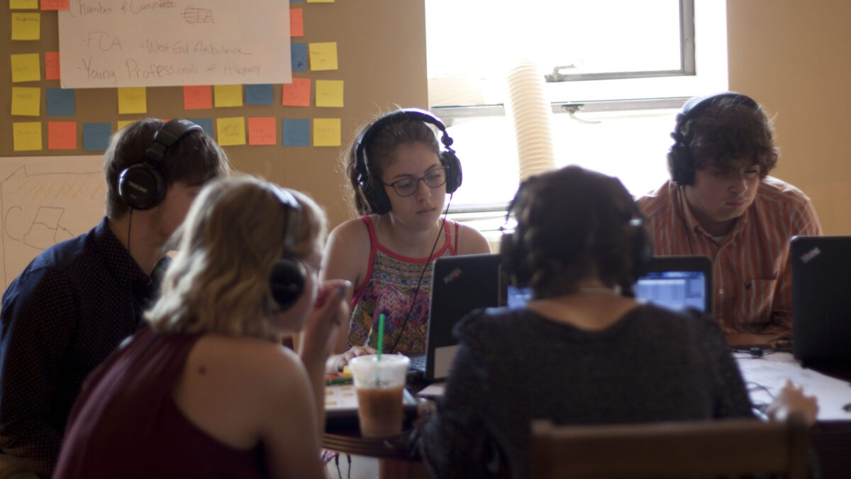 Five teens wearing headphones looking at laptop computers
