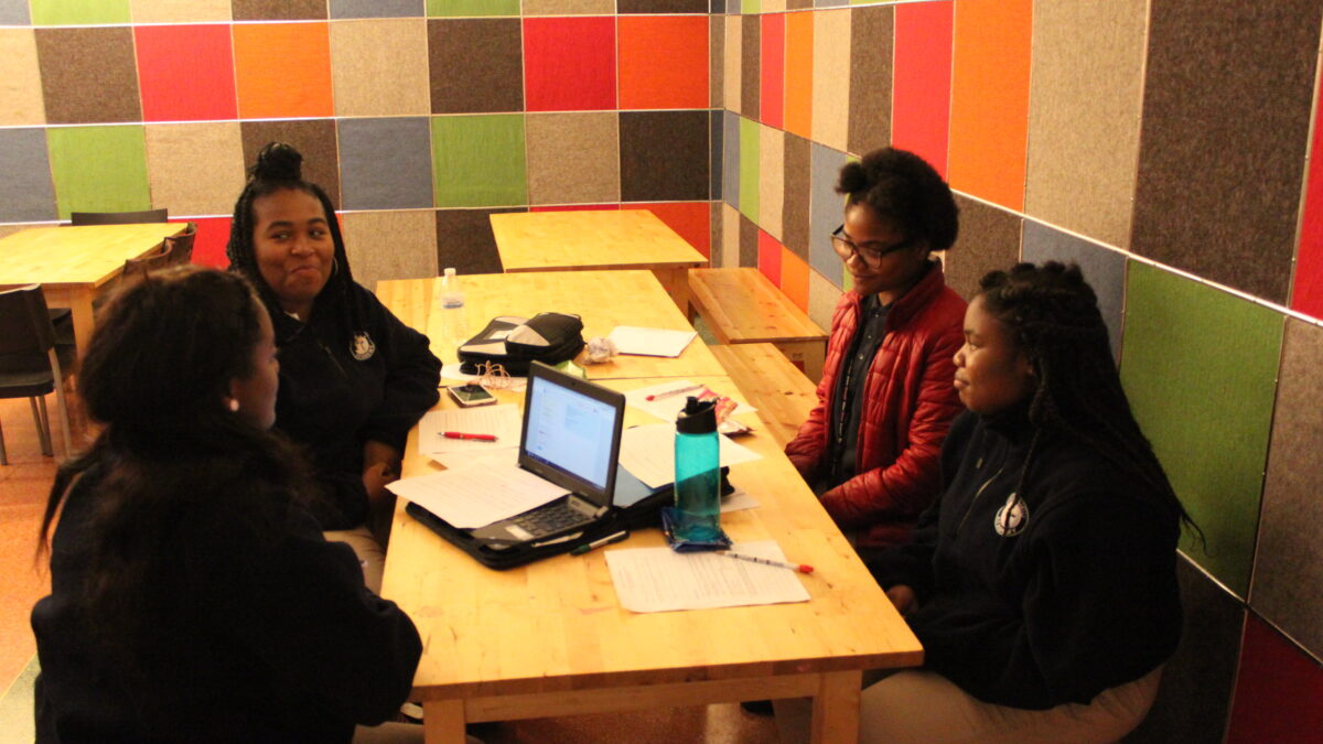 Four youth sitting around a laptop computer and pieces of paper on a wooden table