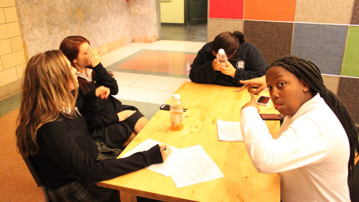 Four youth sitting around pieces of paper on a wooden table