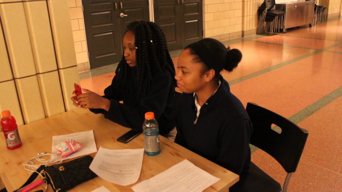 Two youth sitting around pieces of paper and bottles of sports drinks on a wooden table