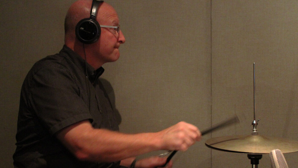 IMG_2101 An adult wearing headphones playing a drum set in a radio studio