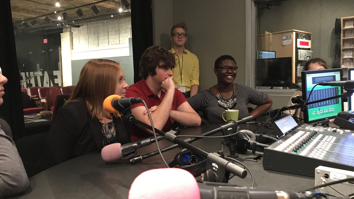 Four teens sitting around microphones in a radio studio