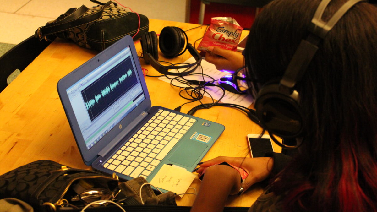 A youth wearing headphones looking at a laptop computer on a wooden table