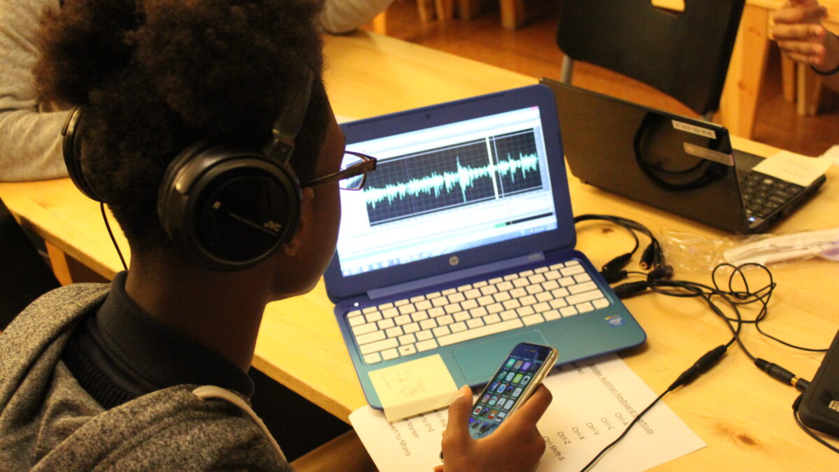 A teen wearing headphones looking at a laptop computer on a wooden table