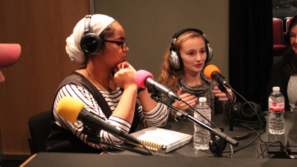 Two youth wearing headphones speaking into microphones being interviewed in a radio studio