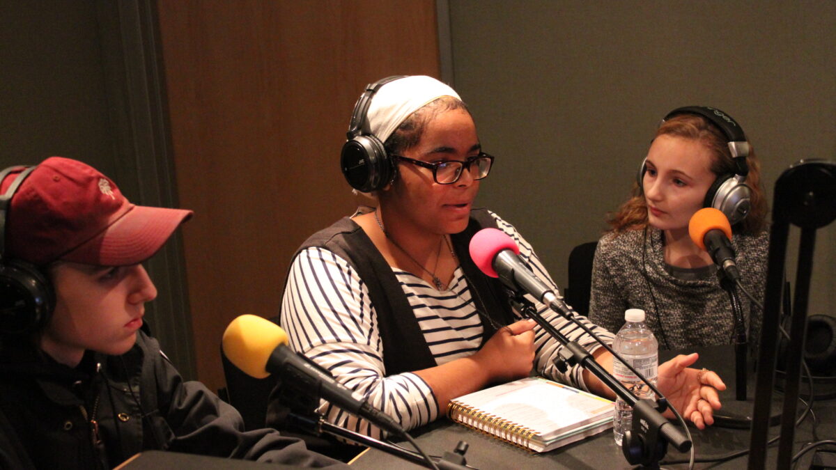 Three teens wearing headphones speaking into microphones in a radio studio