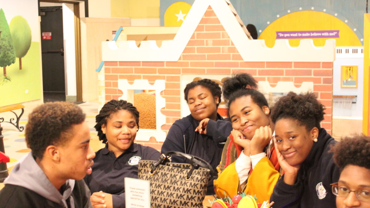 Six teens smiling and sitting in front of a museum exhibit