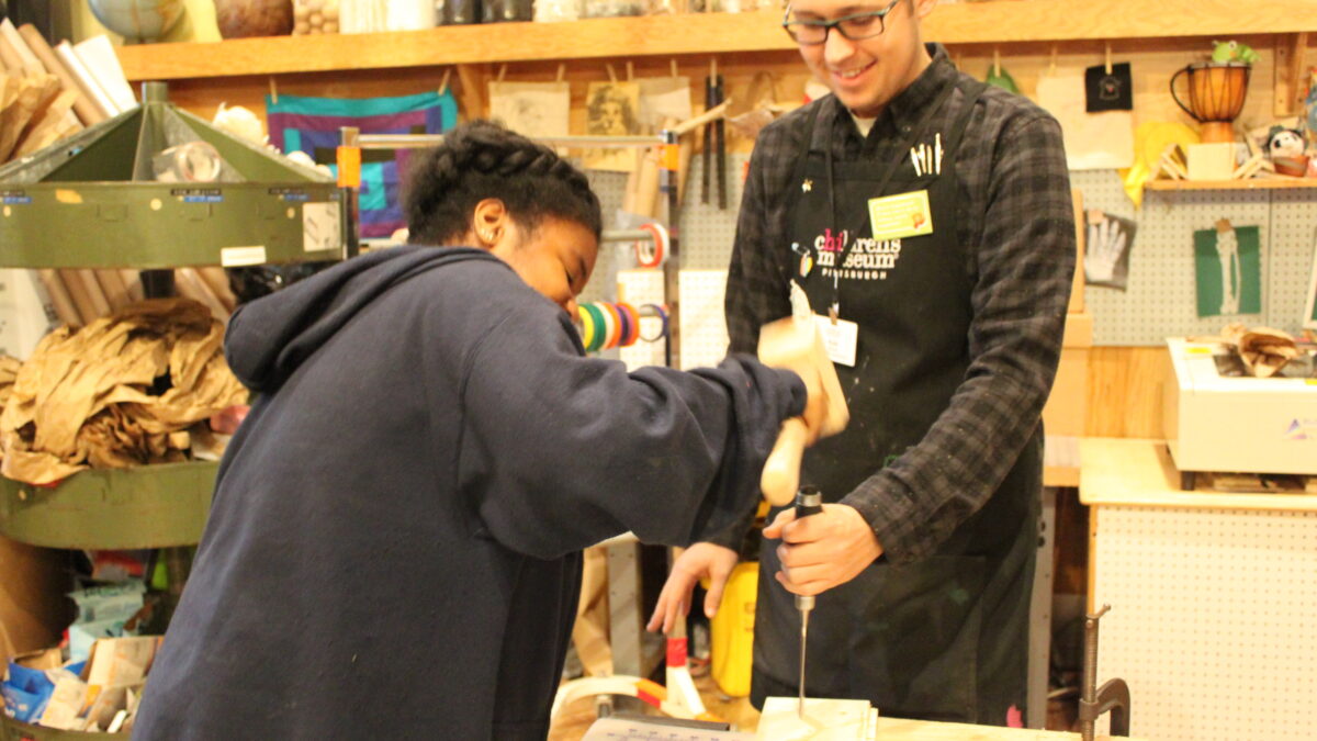 A teen and an adult smiling while working with woodworking tools