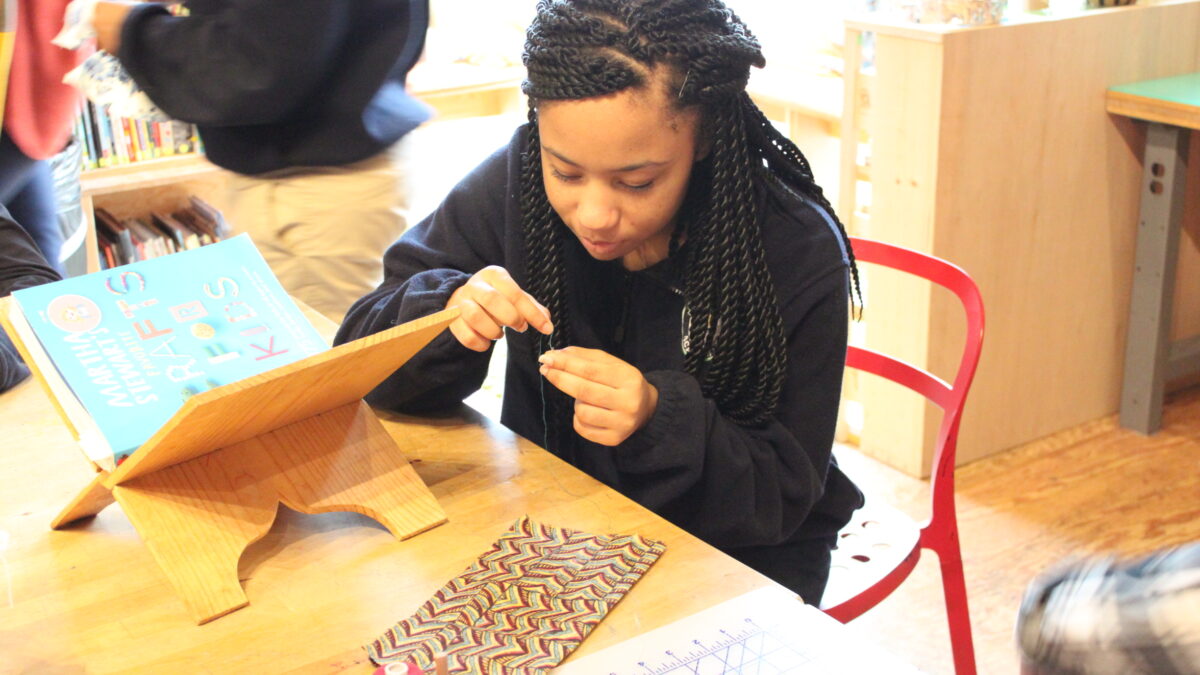 A youth sitting behind a wooden art project on a wooden table