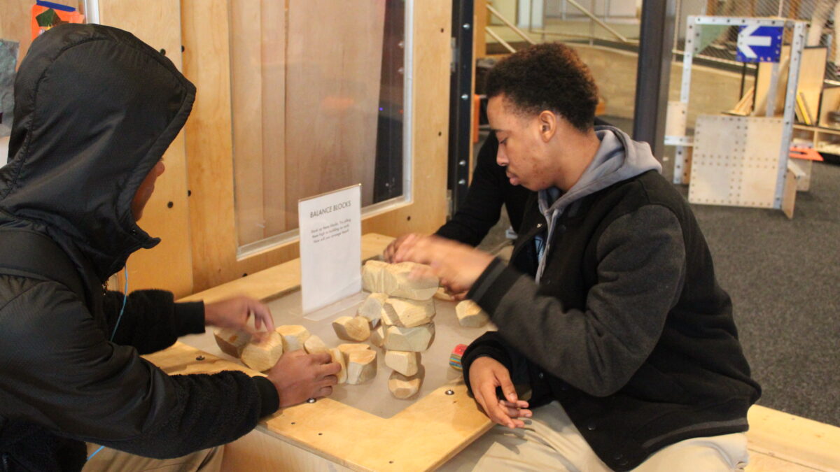 Three teens interacting with a museum exhibit on a wooden table