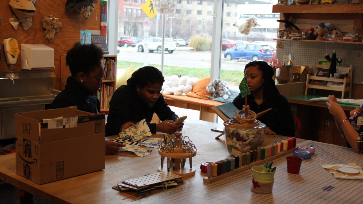 Three teens sitting around a collection of crafted art pieces on a checkered table