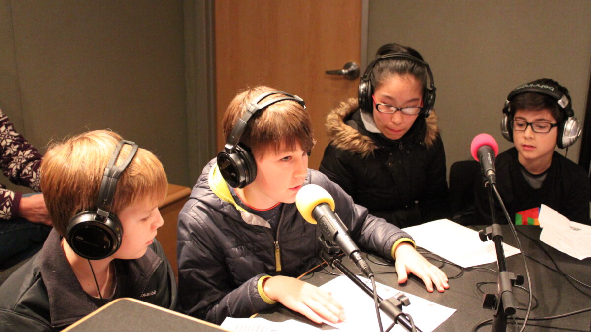 Four youth wearing headphones speaking into microphones in a radio studio