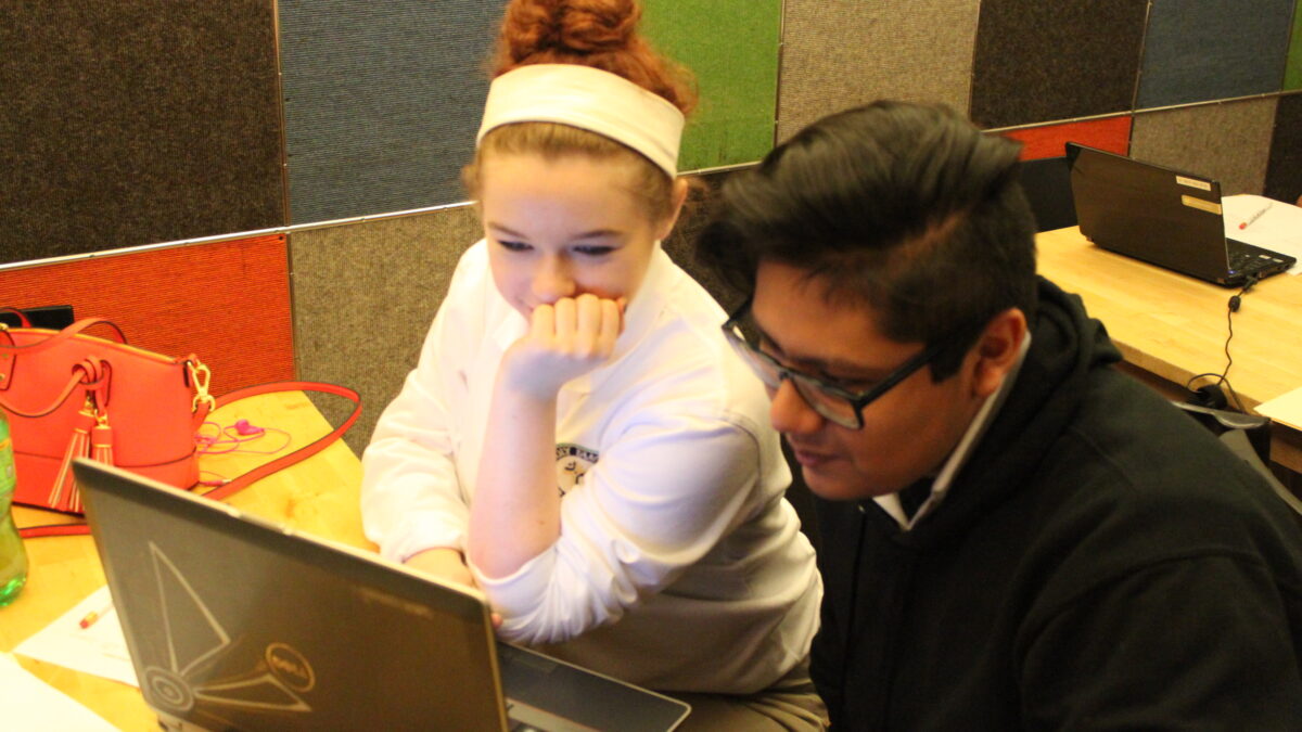 Two teens looking at a laptop computer on a wooden table