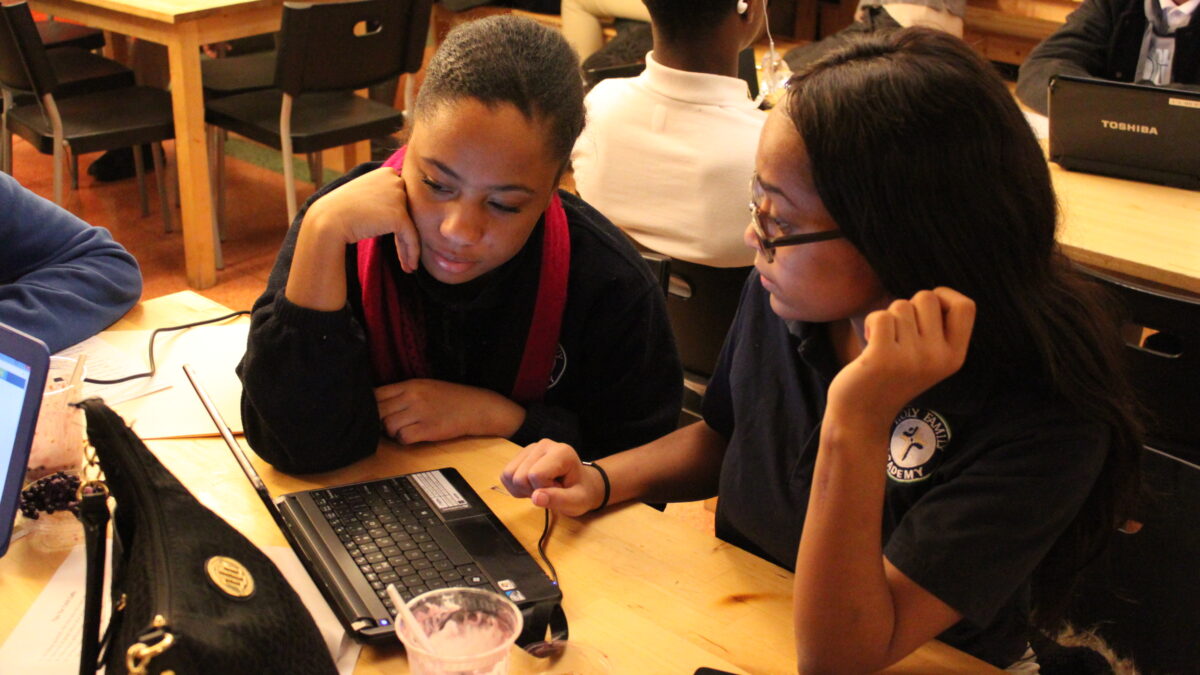Two teens looking at a laptop computer on a wooden table