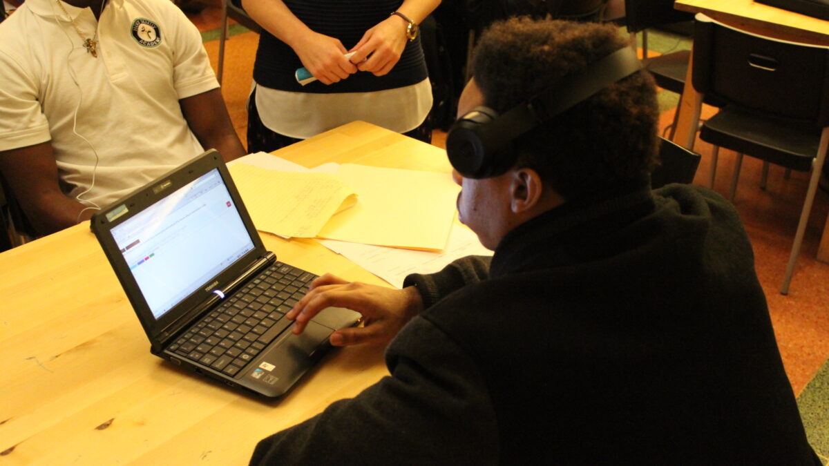 A teen wearing headphones looking at a laptop computer on a wooden table