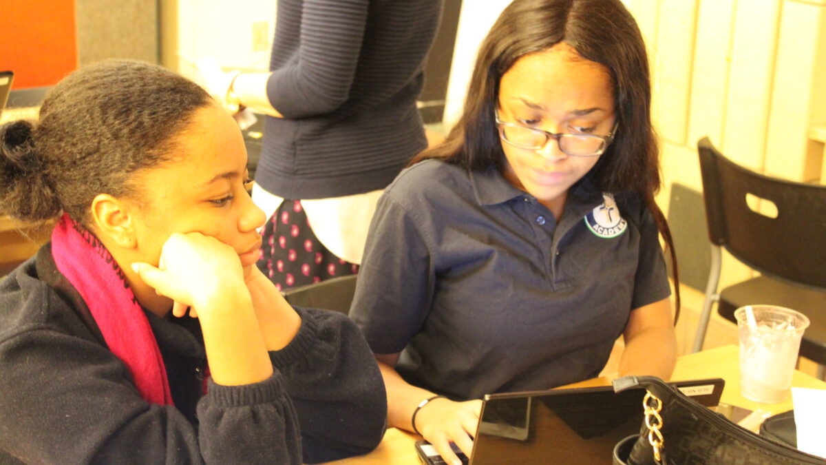 Two teens looking at a laptop computer on a wooden table