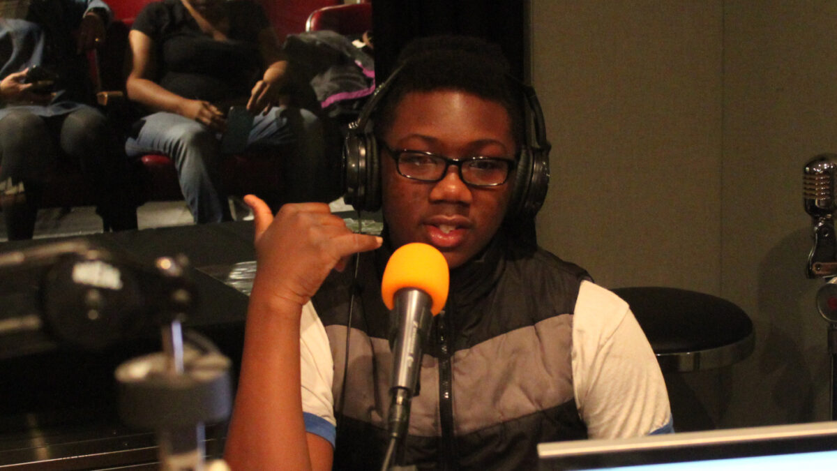 A youth wearing headphones speaking into a microphone in a radio studio