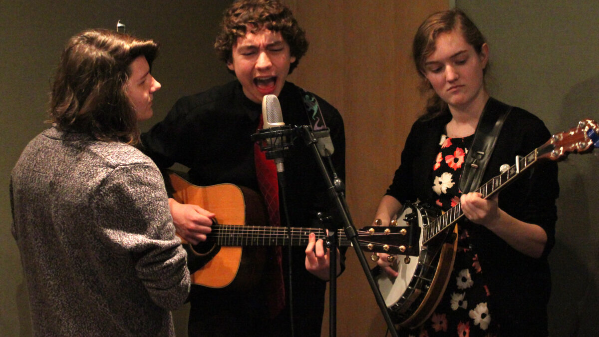 A teen playing a banjo, a teen playing acoustic guitar and singing into a microphone, and a teen singing into a microphone in a radio studio