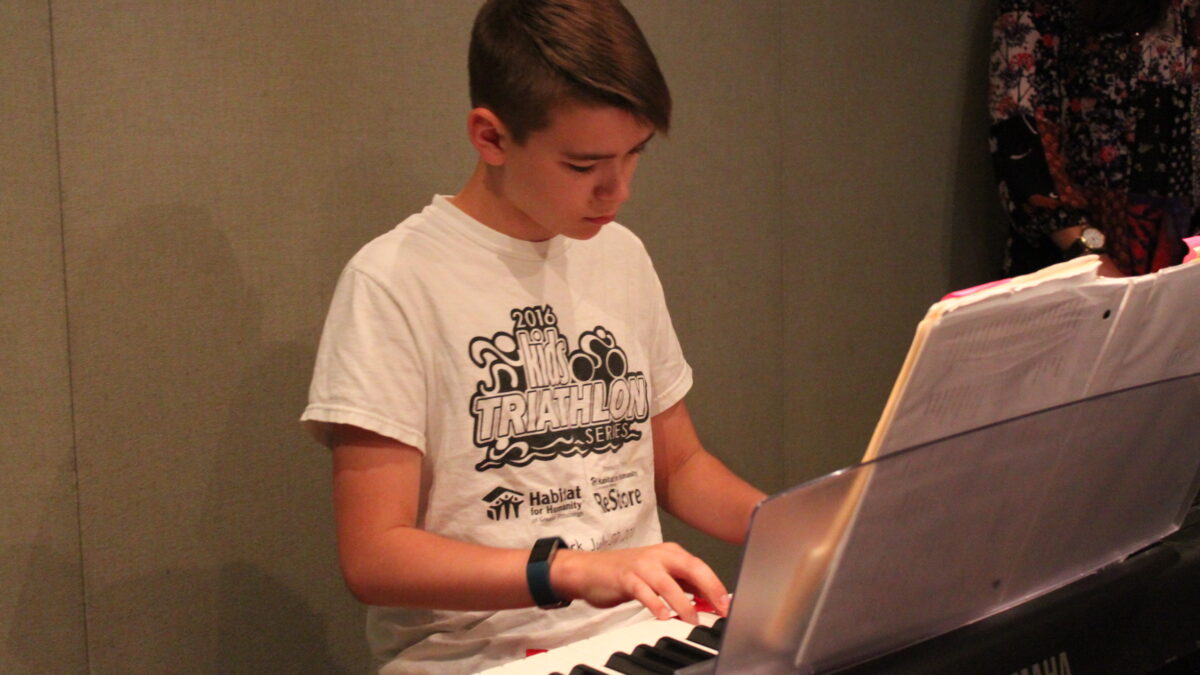 A youth playing a piano keyboard looking at sheet music in a radio studio