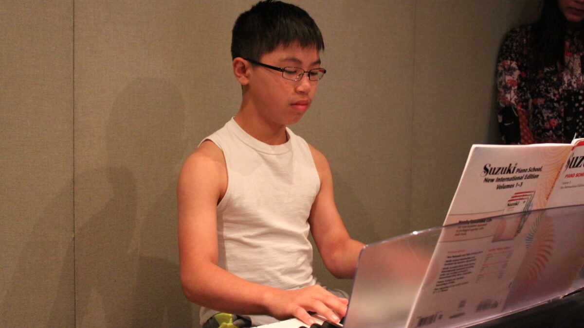 A youth playing a piano keyboard looking at sheet music in a radio studio