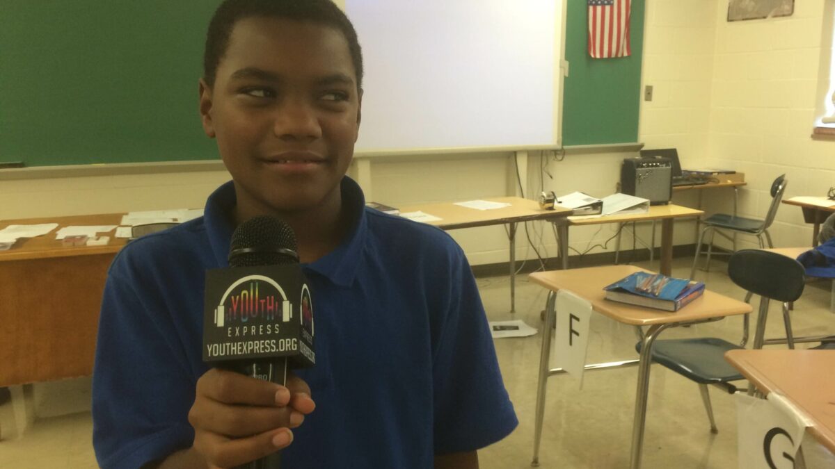 A youth holding a microphone looking off to the side in a classroom