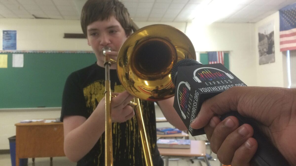 A microphone being held up to a youth playing a trombone