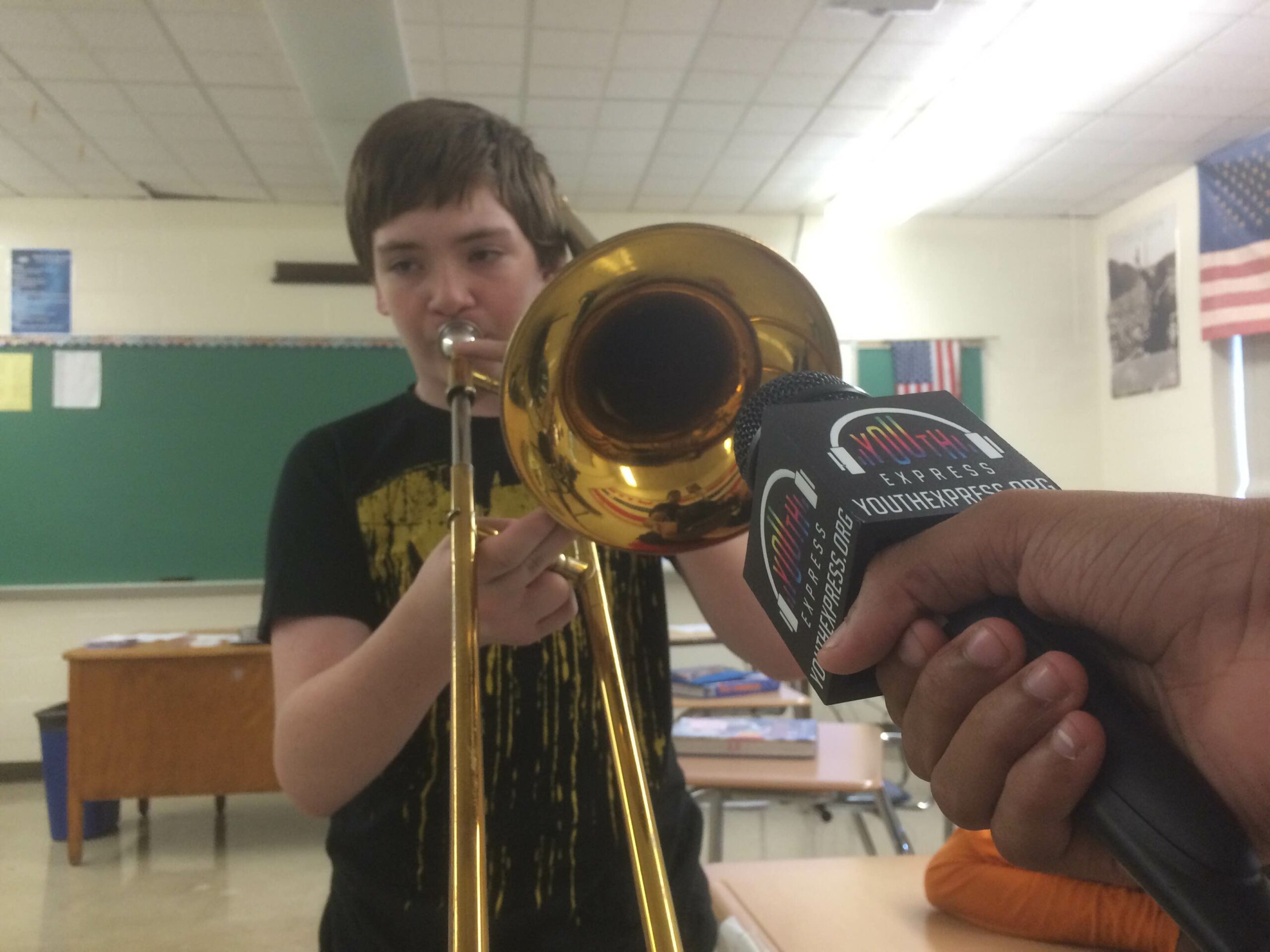A microphone being held up to a youth playing a trombone