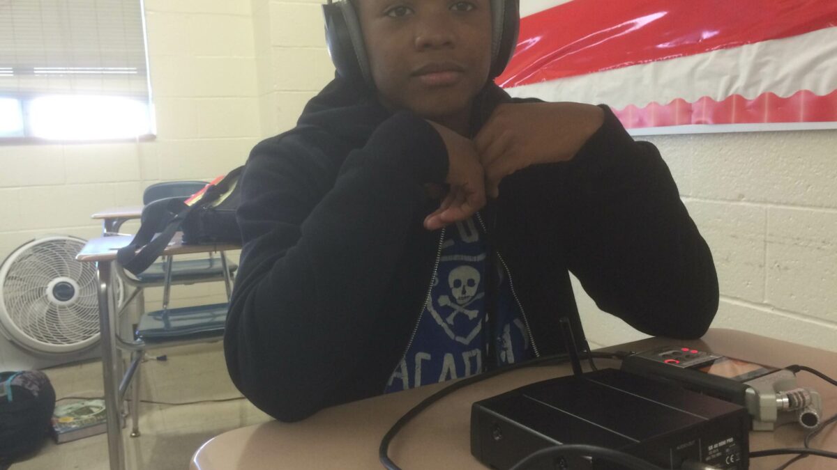 A youth wearing headphones sitting behind a portable recorder in a classroom
