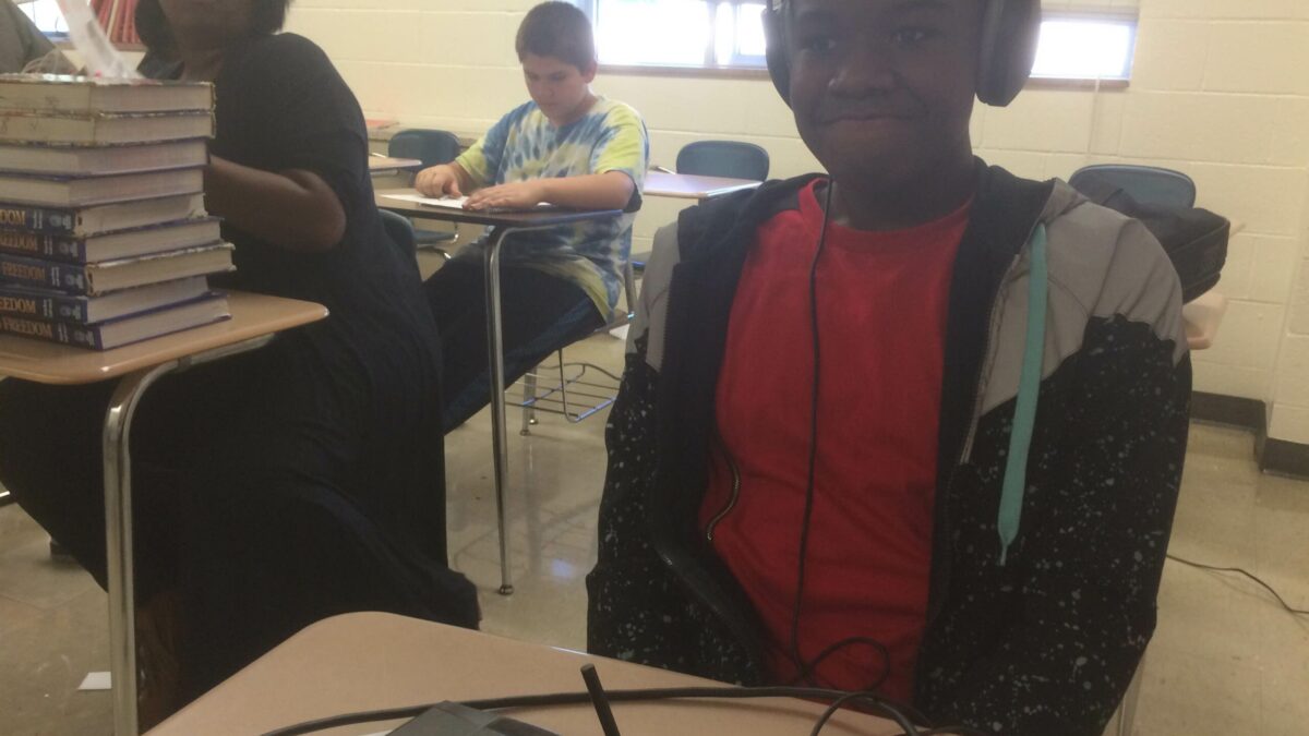 A youth wearing headphones sitting behind a portable recorder on a classroom desk