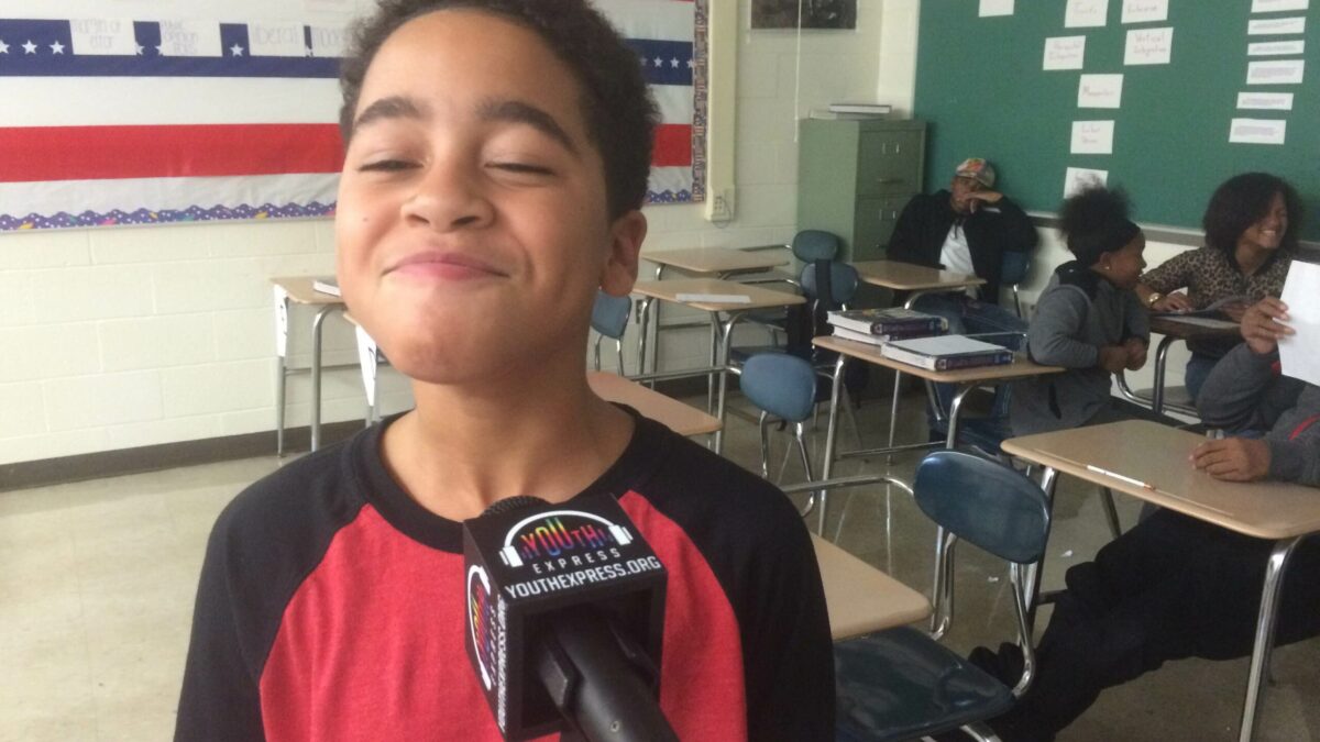 A youth smiling behind a microphone as three youth sit in the background in a classroom