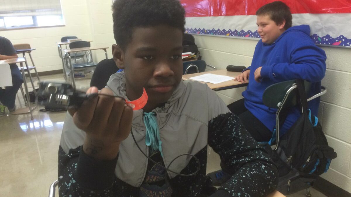 A youth holding a portable recorder sitting at a classroom desk