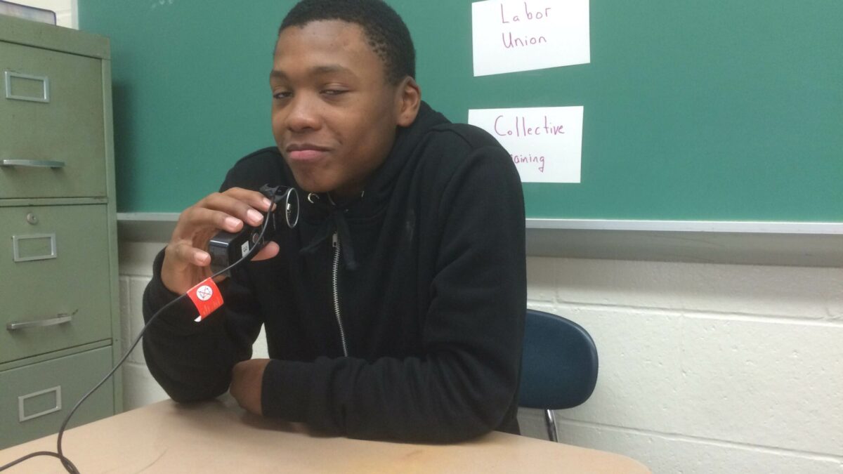 A youth holding a microphone sitting in a classroom