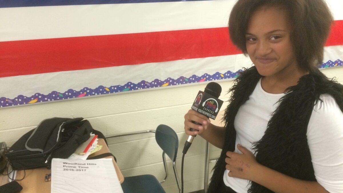 A youth smirking while holding a microphone in a classroom