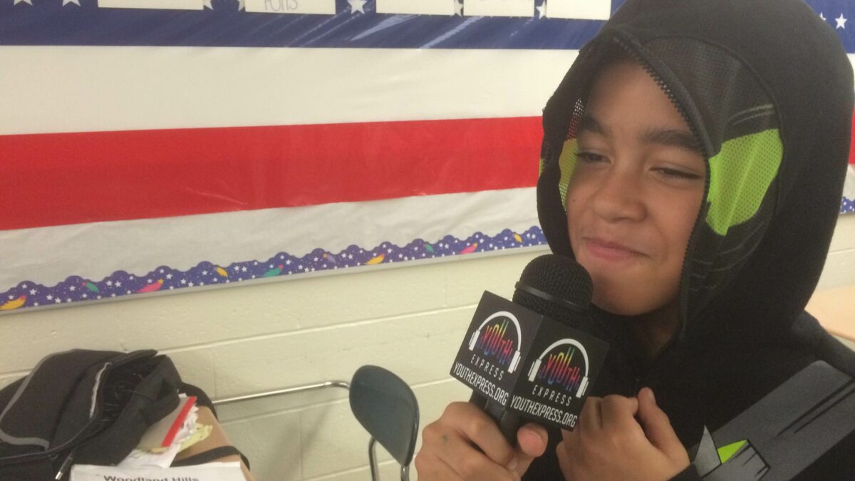 A youth wearing a hoodie holding a microphone in a classroom
