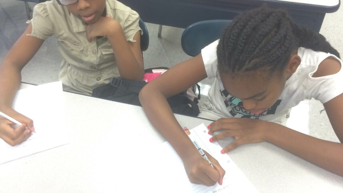 Two youth writing on pieces of paper in a classroom