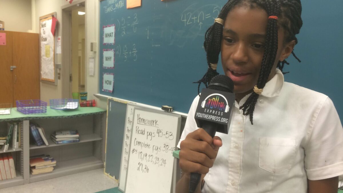 A youth holding and speaking into a microphone in a classroom
