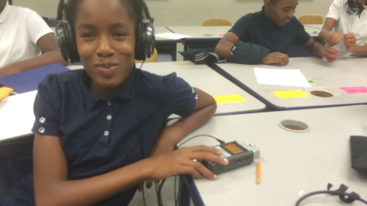 A youth wearing headphones connected to a portable recorder in a classroom