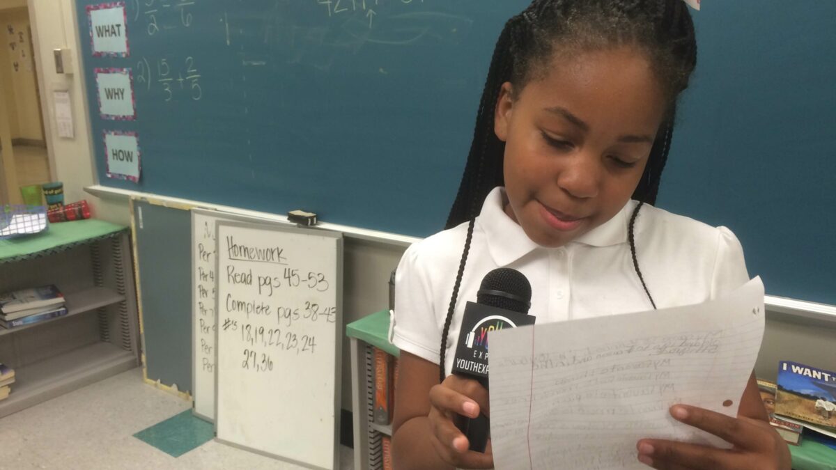 A youth looking at a piece of paper speaking into a microphone in a classroom