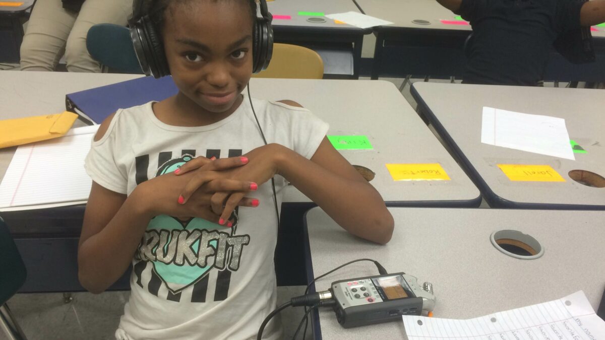 A youth wearing headphones connected to a portable recorder sitting in a classroom