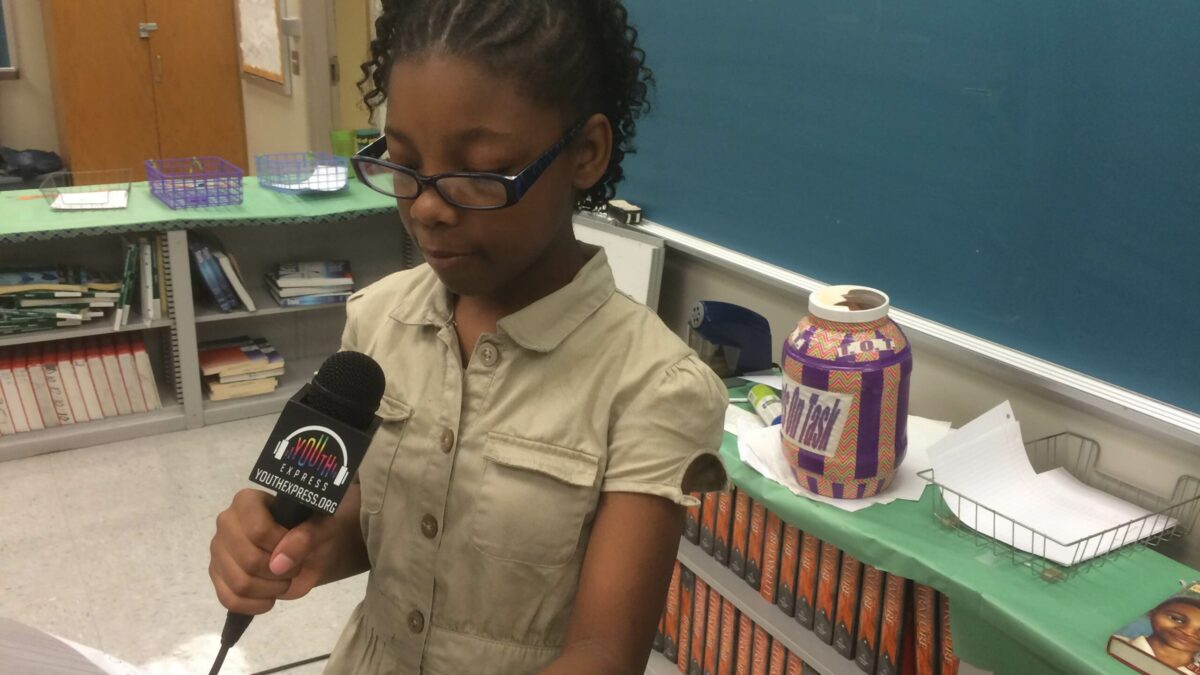 A youth holding a piece of paper speaking into a microphone in a classroom