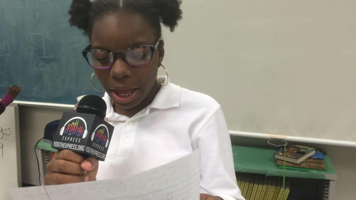 A youth holding a piece of paper and speaking into a microphone in a classroom