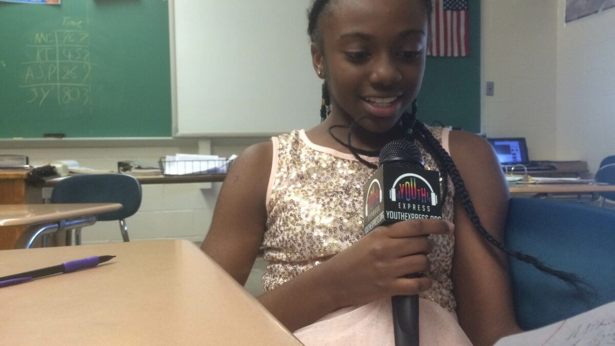A youth holding a piece of paper and speaking into a microphone in a classroom