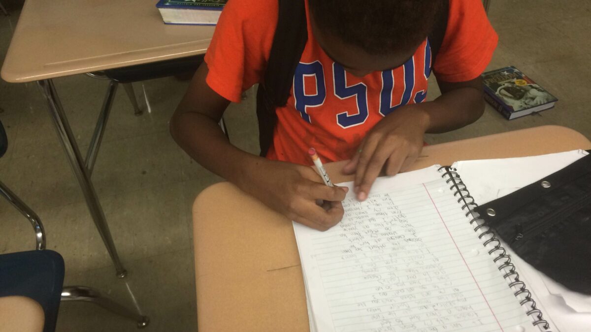 A youth writing into a notebook in a classroom