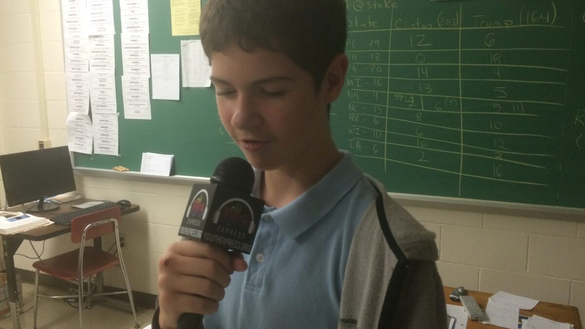 A youth holding and speaking into a microphone in a classroom