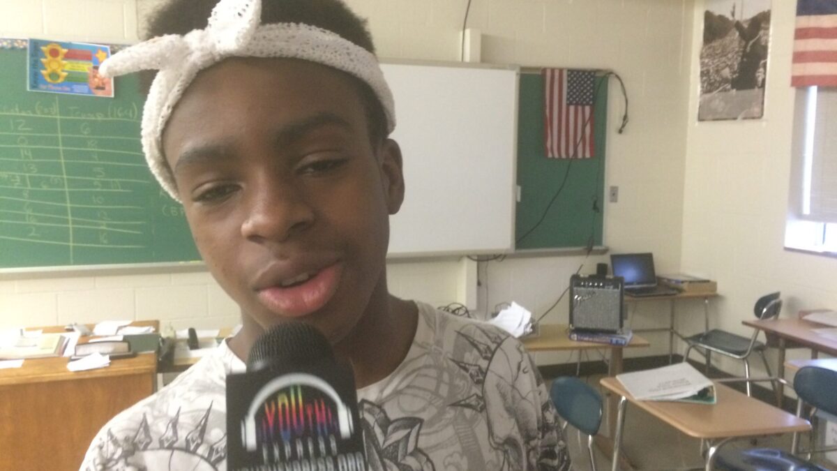 A youth holding and speaking into a microphone in a classroom