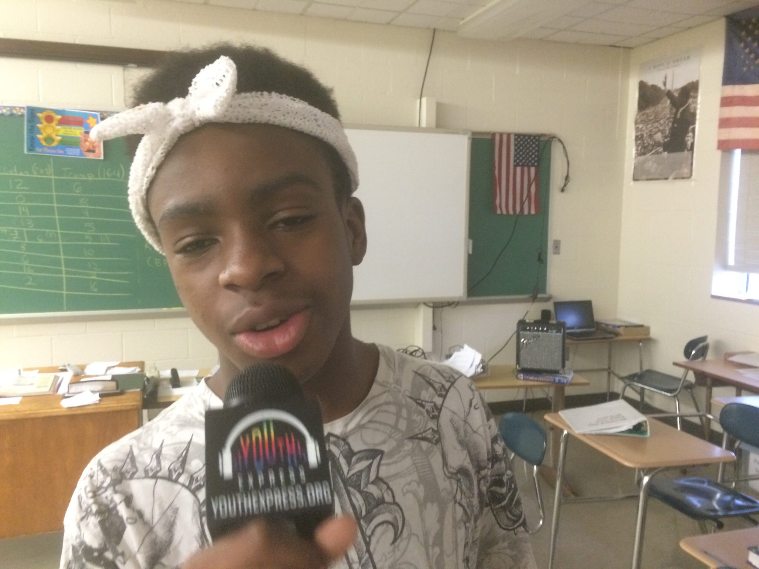 A youth holding and speaking into a microphone in a classroom
