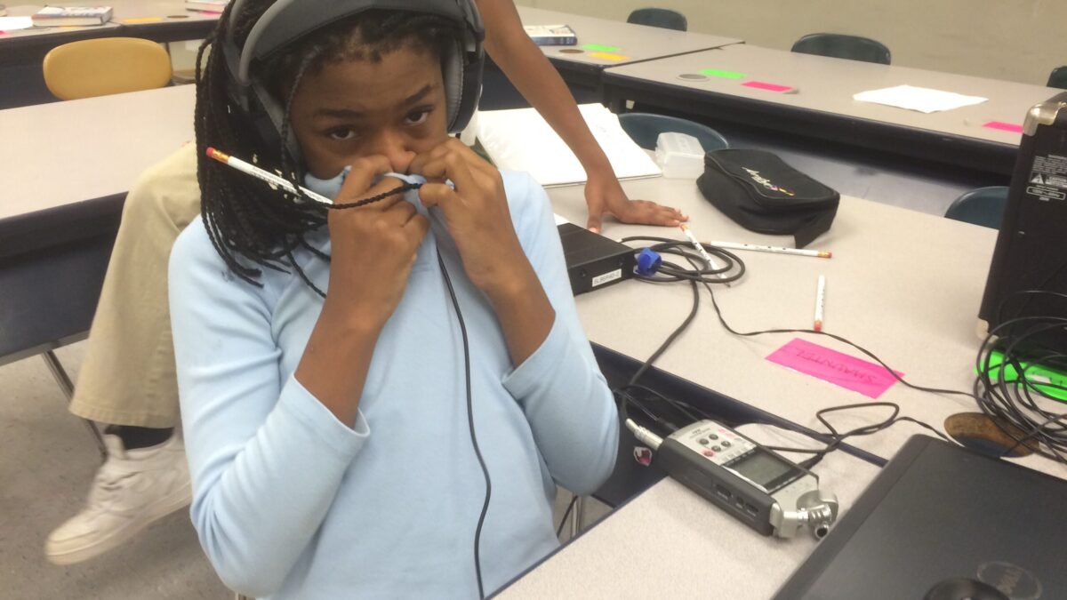 A youth wearing headphones holding their shirt up to their nose in a classroom
