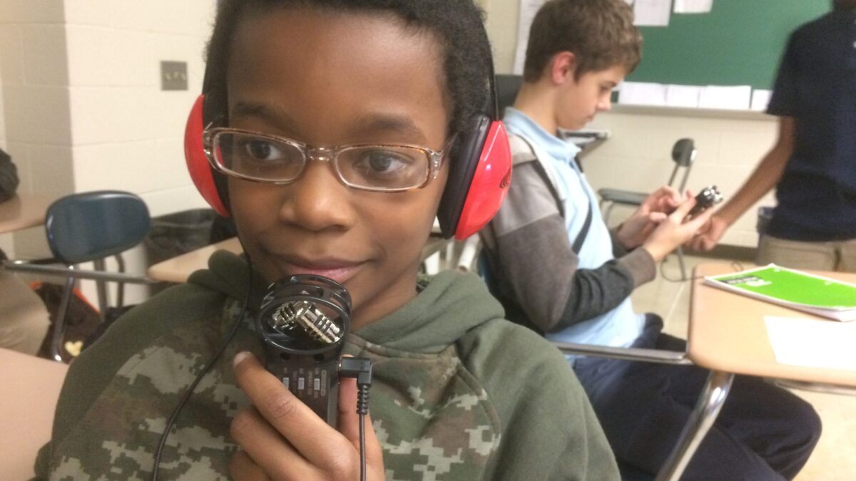 A youth wearing headphones holding a portable recorder